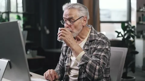 Handsome gray haired businessman drinking clean water from glass while working Stock Footage 253513712