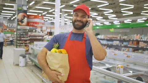 Handsome grocery delivery man talking to mobile and holding grocery paper bag Stock Footage 93545203