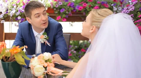 Handsome groom telling something to his beautiful bride sitting at a table in Stock Footage 63994611