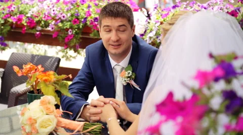 Handsome groom telling something to his beautiful bride sitting at a table in Stock Footage 63995685
