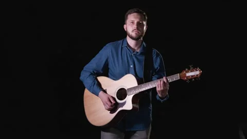 Handsome guy with beard playing acoustic guitar. Black background. Isolated Stock Footage 135234407