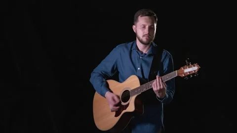 Handsome guy with beard playing acoustic guitar. Black background. Isolated Stock Footage 135234515