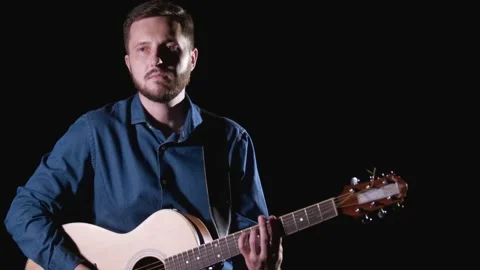 Handsome guy with beard playing acoustic guitar. Black background. Isolated Stock Footage 135234566