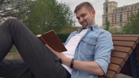 The handsome guy closing the book. The young man sits in the park. Man finish Stock Footage 89448212