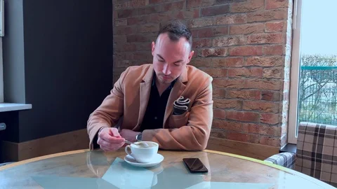 Handsome guy drinks big coffee alone in a cafe Stock Footage 128537353