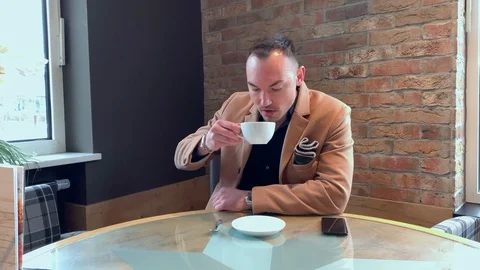 Handsome guy drinks big coffee alone in a cafe Stock Footage 128537513