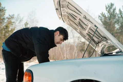 Handsome guy fixing a car under a hood in sunny winter day Stock Photos