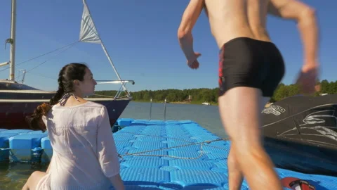 Handsome guy with girlfriend having fun on the pier and jumping into the water Stock Footage 124805714