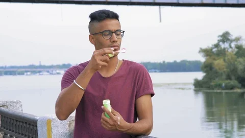 Handsome Guy with Hipster Prick Starts Soap Bubbles on the River Embankment Stock Footage 95409904