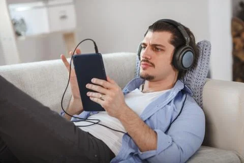 Handsome guy lying on sofa with tablet and headphones Foto stock