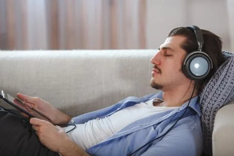 Handsome guy lying on sofa with tablet and headphones Stock Photos