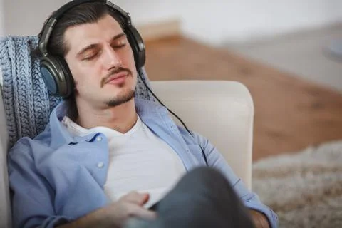 Handsome guy lying on sofa with tablet and headphones Stock Photos