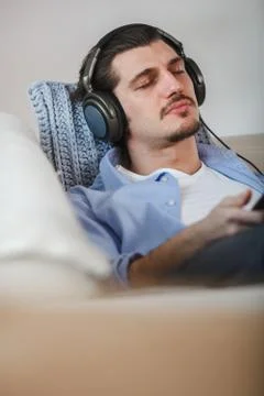Handsome guy lying on sofa with tablet and headphones Stock Photos