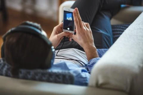 Handsome guy lying on sofa with tablet and headphones Stock Photos