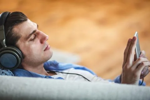 Handsome guy lying on sofa with tablet and headphones Stock Photos