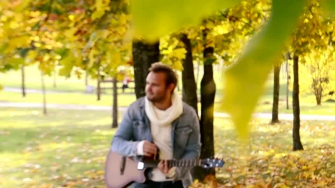 Handsome guy playing guitar in autumn Park Stock Footage 144123887