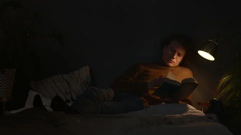 Handsome guy is reading book at night lying under the lamp Stock Footage 146310783