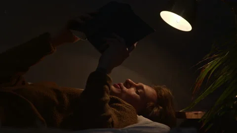 Handsome guy is reading out loud book at night lying under the lamp Stock Footage 146309536