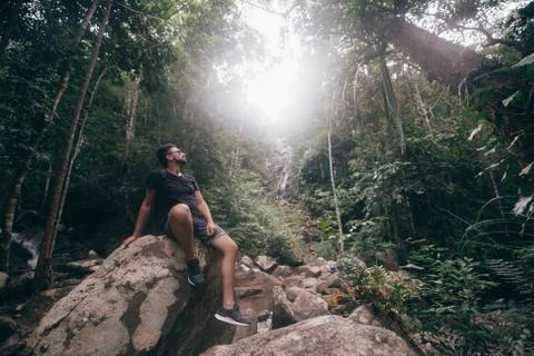 Handsome guy on the rocks at a tropical waterfall. Stock Photos