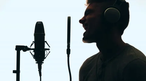 Handsome guy singing into a microphone standing backlit. Recording studio. Man Stock-Footage 58628247
