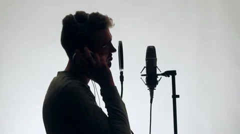 Handsome Guy Sings in a Microphone Standing studio headphones. The guy standing Stock Footage 58628311