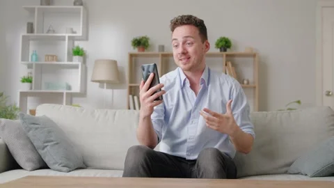Handsome guy sit on sofa holding smartphone use videocall app enjoy personal Stock Footage 169017779