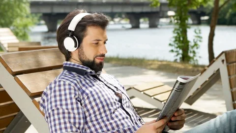 Handsome guy is sitting and holding journal. He is looking at it and smiling Stock-Footage 99739833
