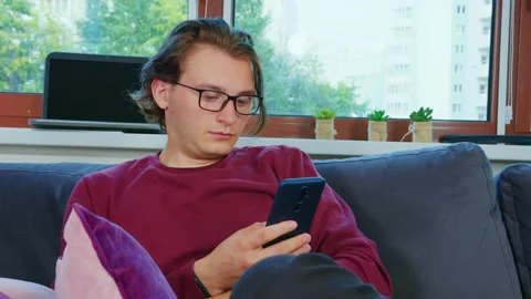 Handsome guy sitting on couch, using cell phone Video stock 165994846