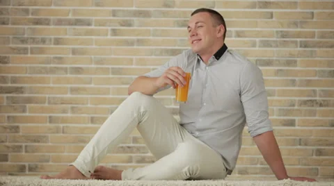 Handsome guy sitting on floor drinking juice and smiling Video stock 28389839