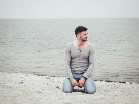 Handsome guy sitting on the sand on the beach Stock Photos