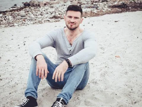 Handsome guy sitting on the sand on the beach Stock Photos