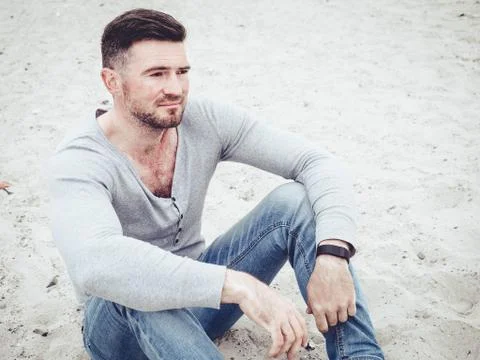 Handsome guy sitting on the sand on the beach Stock Photos