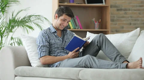 Handsome guy sitting on sofa reading book and smiling Video stock 28792973