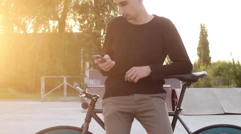 Handsome Guy Type a Message Standing Near a Bicycle at Sunset. Stock-Footage 62852960