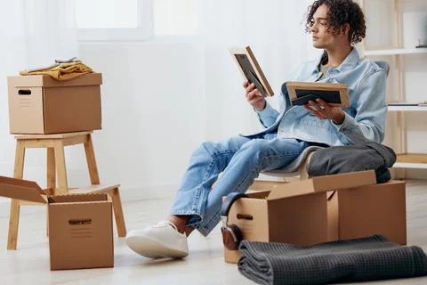 Handsome guy unpacking things from boxes in the room sorting things out Stock Photos