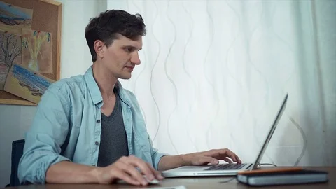 Handsome guy using laptop at office. Board with color sketches at wall behind Video stock 79901887
