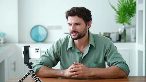 Handsome guy using mobile phone mounted on tripod, talking by video link Stock Footage 213259282