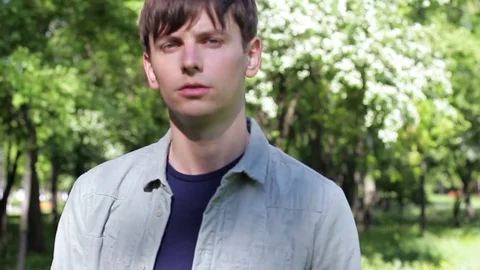 A handsome guy walks through the park. He comes closer and looks at the c Stock Footage 75549948