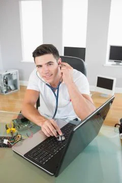 Handsome happy computer engineer examining laptop with stethoscope Stock Photos