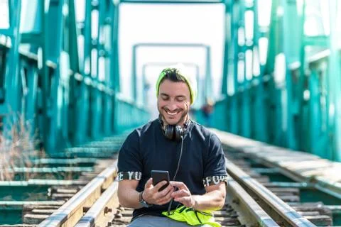 Handsome Hipster Guy Using the Cellphone and Wearing Headphones. Sitting on t Stock Photos