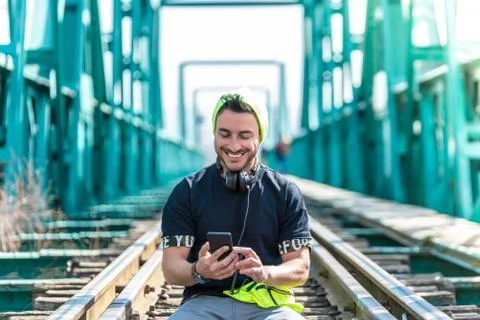 Handsome Hipster Guy Using the Cellphone and Wearing Headphones. Sitting on t Stock Photos