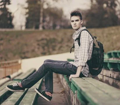 Handsome hipster man model with backpack and stylish hair in the city, street Stock Photos
