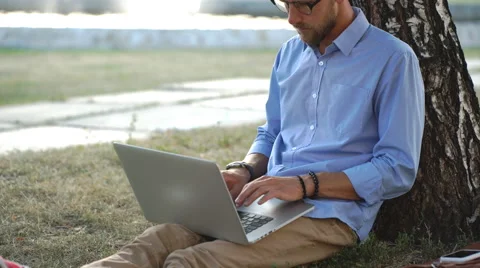 Handsome hipster using laptop in park on a summers day Stock Footage 68078073