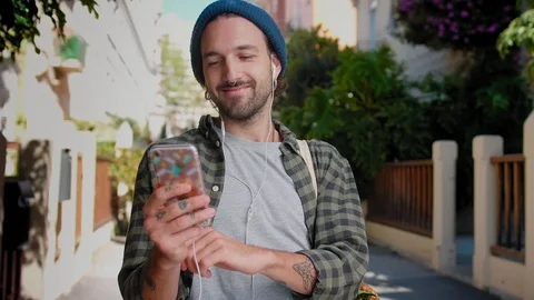 Handsome Hispanic guy smiling and using smartphone device online at cozy city Stock Footage 111071137
