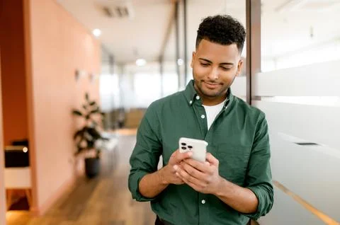 Handsome hispanic guy is using smartphone for messaging, texting, young dark Stock Photos