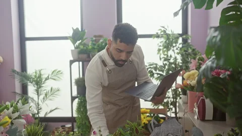 Handsome hispanic man using laptop amid vibrant flowers indoors at a floris.. Stock Footage 282585509