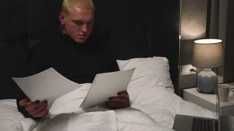 Handsome homosexual man working with Documents on Bed before going to sleep at Video stock 146906681