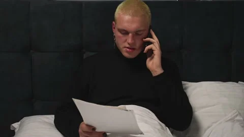 Handsome homosexual man working with Documents on Bed, talking on phone before Stock Footage 146907380