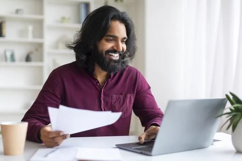 Handsome Indian freelancer guy working on his laptop and checking documents 写真素材