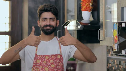 Handsome Indian man happily gesturing thumbs-ups while standing in the kitchen Stock Footage 199018839